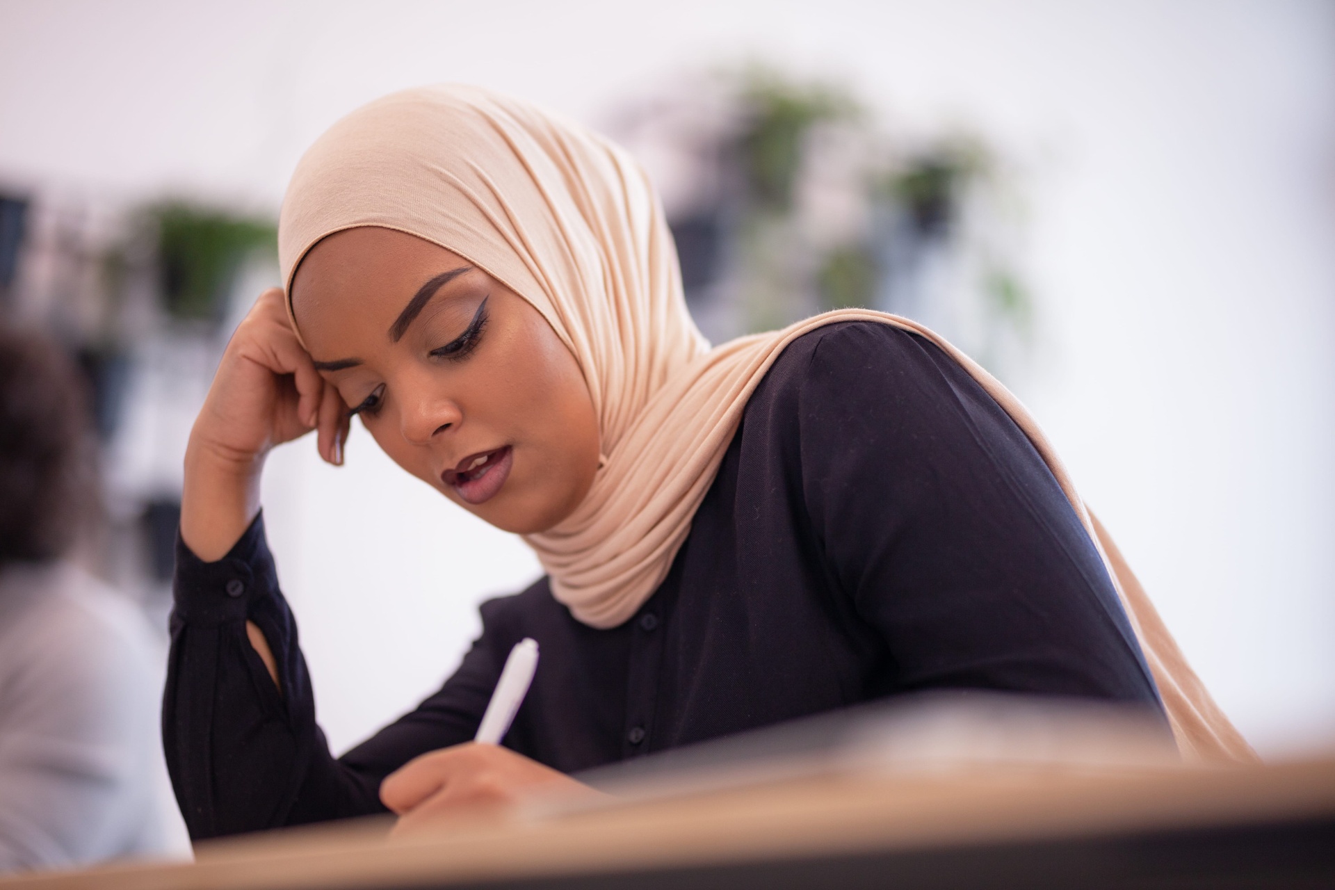 A woman in hijab writing reflectively in a peaceful setting