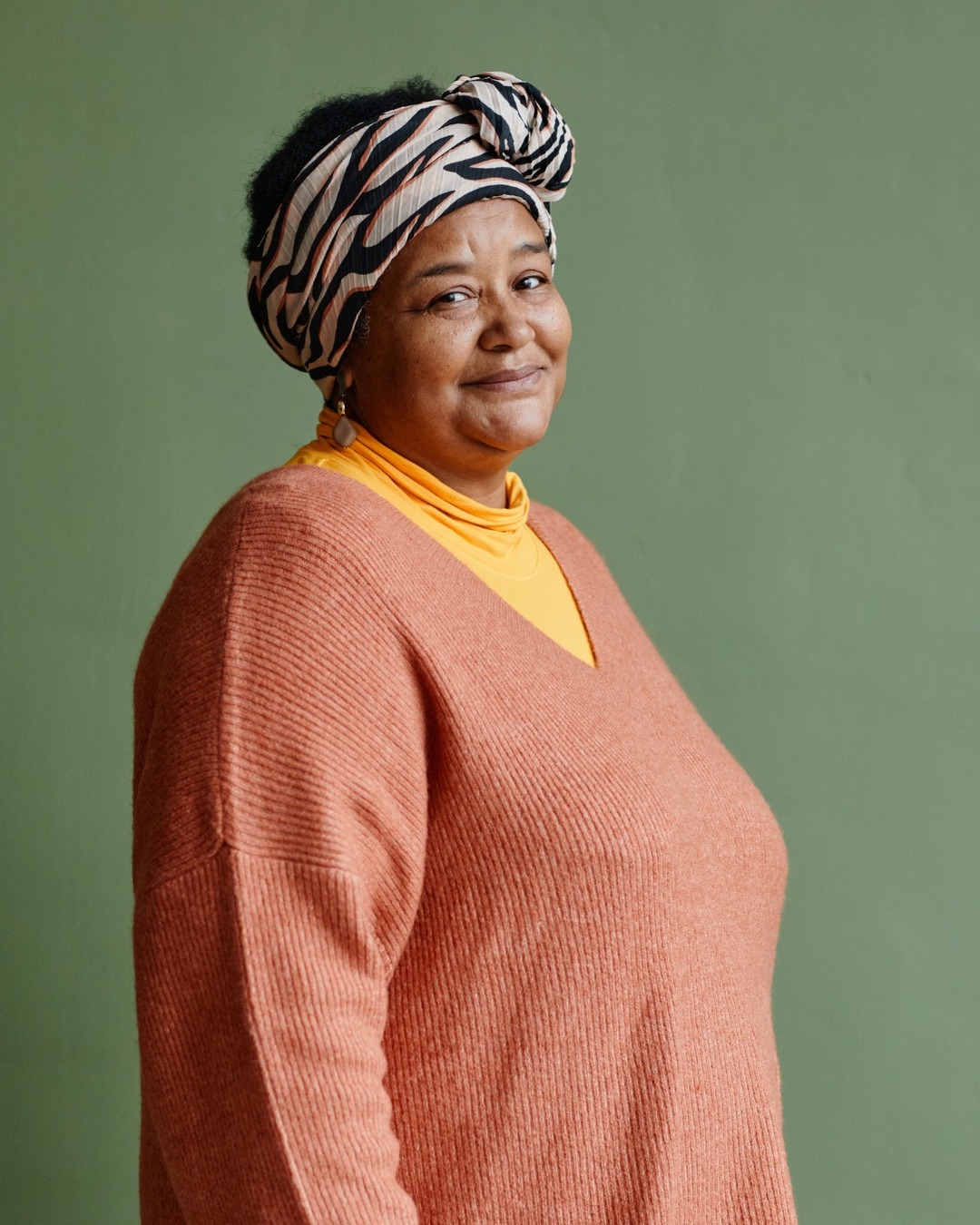 A Muslim woman in a headwrap and warm sweater, smiling gently