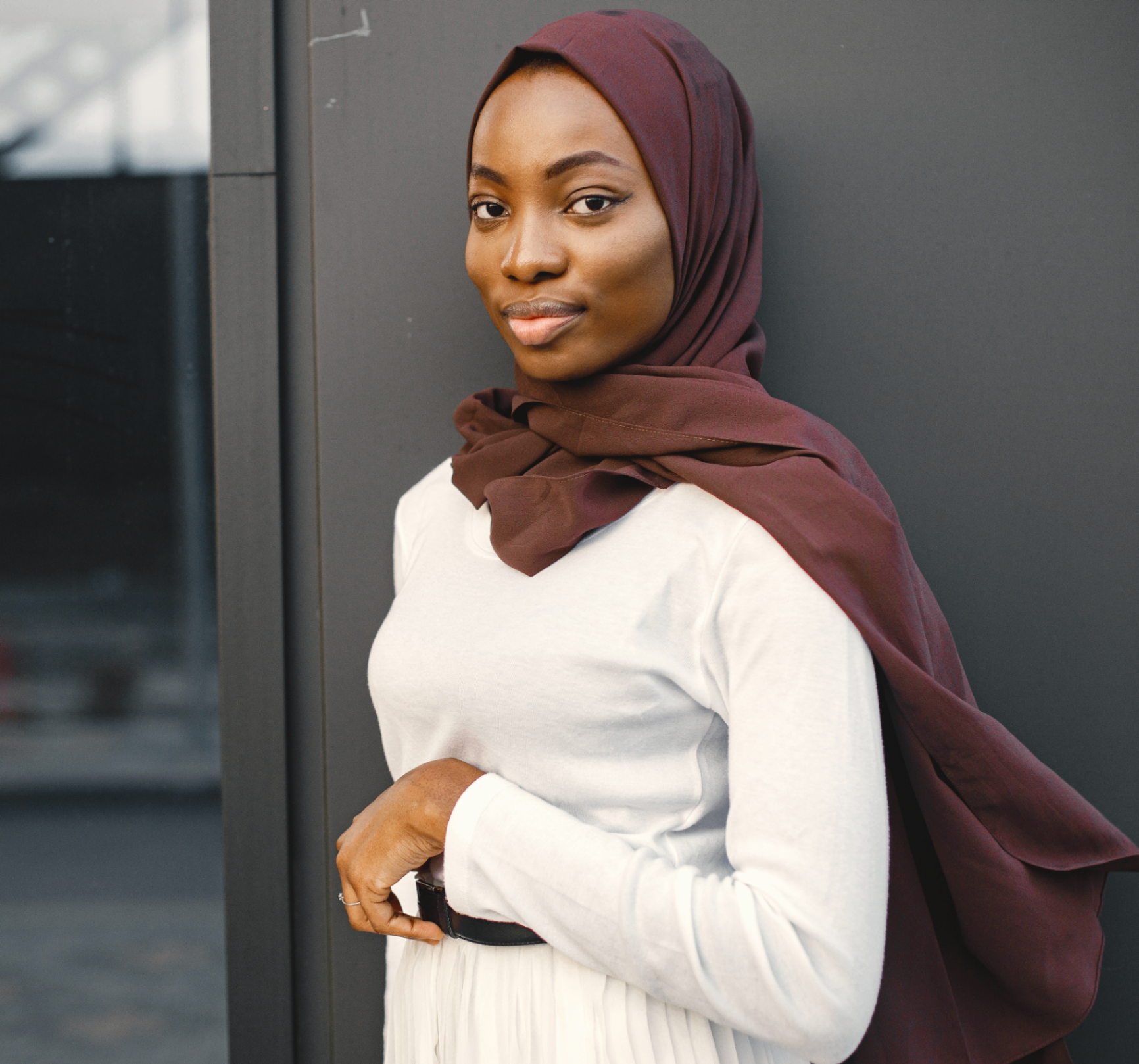 A Muslim woman in a burgundy hijab and white top, looking softly at the camera