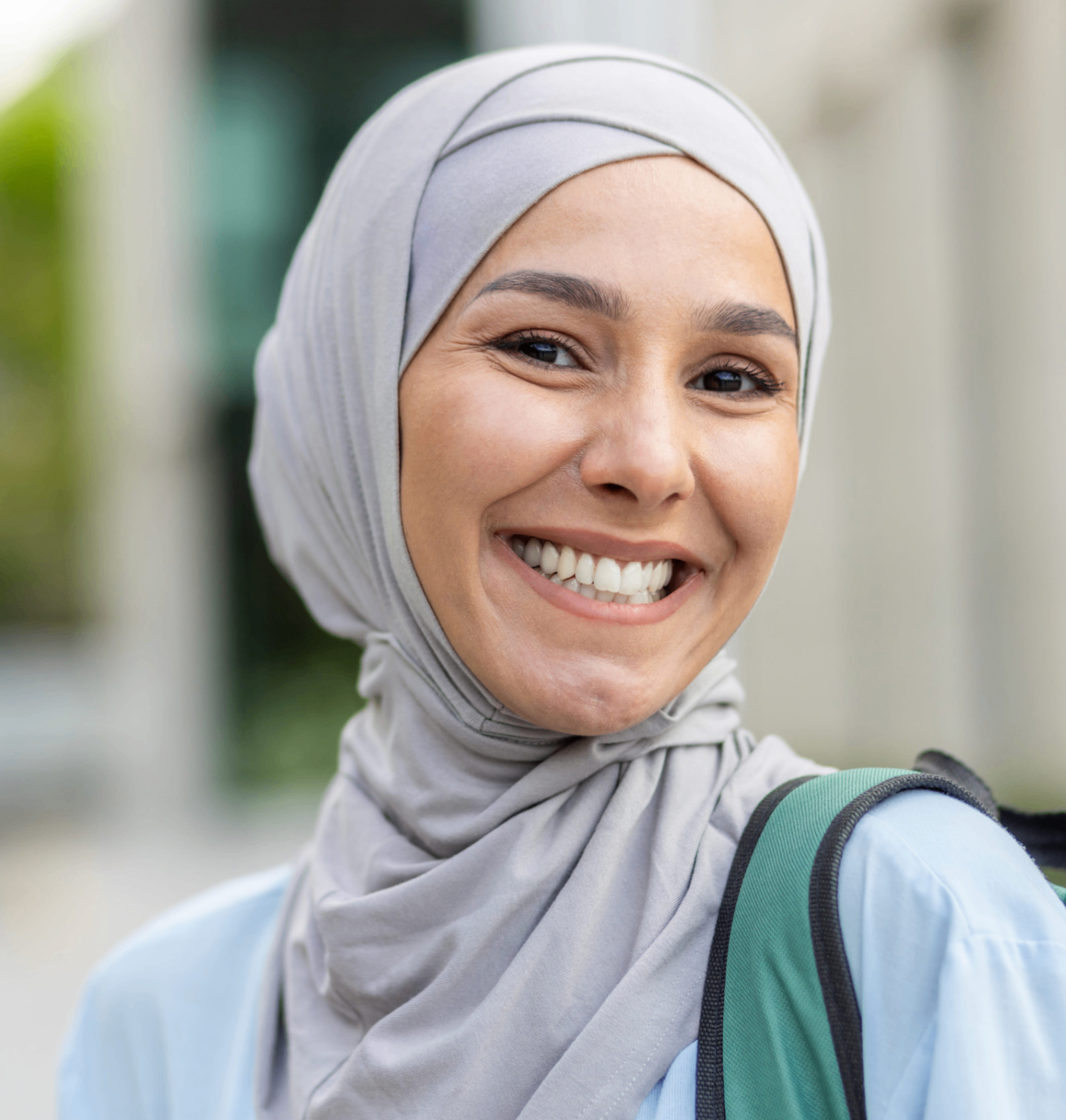 A woman in a grey hijab smiling brightly in daylight