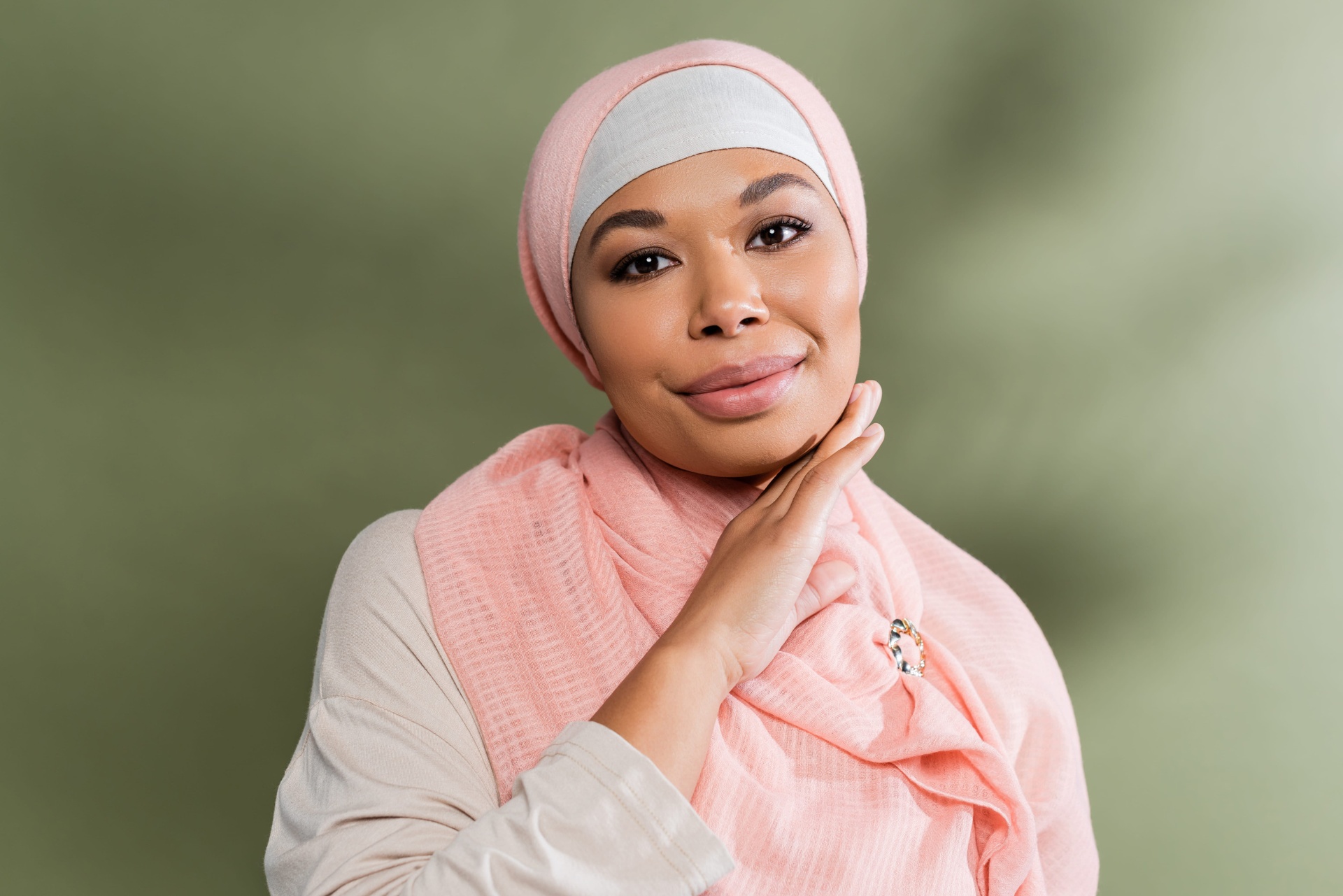 A Muslim woman in a soft pink hijab, resting her hand beneath her chin